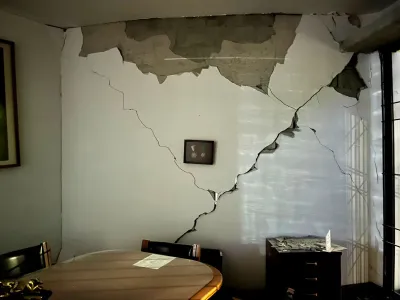 A frame with two medals hangs on a wall that has major cracks on it in a conference room. 
