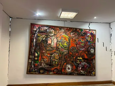 A large-scale painting is titled and hangs from a cracked wall. 