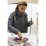 Portrait of Kerstin Brätsch holding a paintbrush and staring down at a painting in progress.