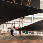 Three people, who look minuscule, look at a massive black sculpture.