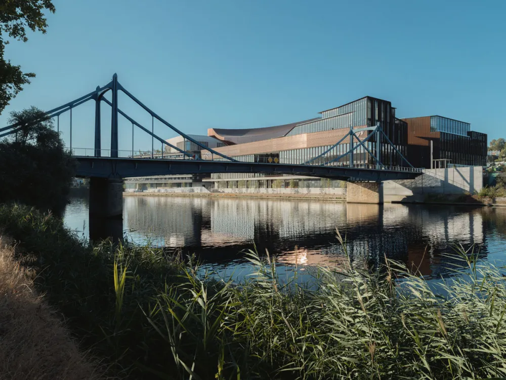 View of a museum building in the distance with wild grass and the Seine in the foreground and a bridge in the middle ground.