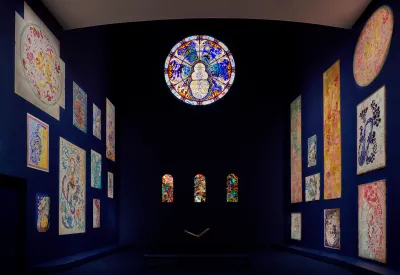 View of an museum exhibition with carpets on the left and right walls and one large circular and three small window stained glass on the center wall. 