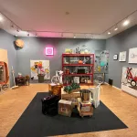An exhibition space made to look like a utility closet, with paintings leaned against its walls and clustered in its center.
