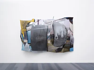 A wall-hung sculpture of various photos affixed to multiple pieces of metal assembled to look like a scrunched-up car.