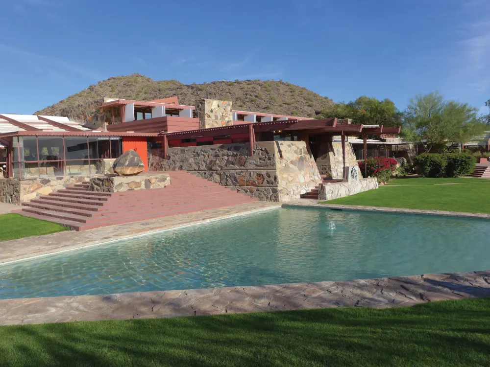 A geometric stone building in front of a blue pond.