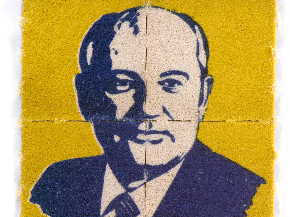 A perforated piece of paper shows a stylized image of Mikhail Gorbachev on a yellow background.