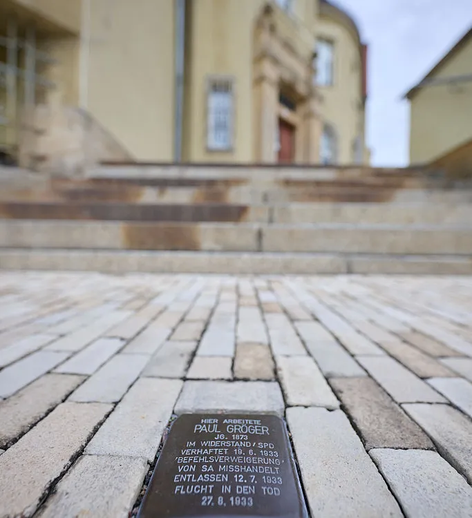 A Stolperstein commemorating Nazi victim Paul Gröger is embedded in the sidewalk in front of City Hall in Saxony, Heidenau, 2026.