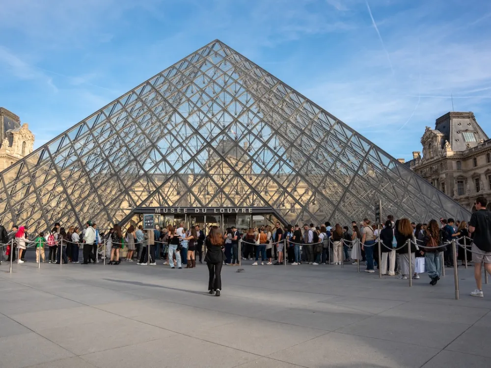 A line of people in front of a glass pyramid.