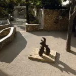 Sunlit sculpture garden at the Fondation Maeght in southern France, featuring abstract sculptures, stone walls, and a colorful mosaic mural.