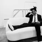 black and white photo of a man in a dark suit and white shirt and sneaker lounging on a white couch
