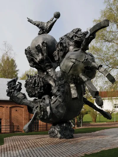 An abstract sculpture that could be a figure holding a ball installed outdoors.