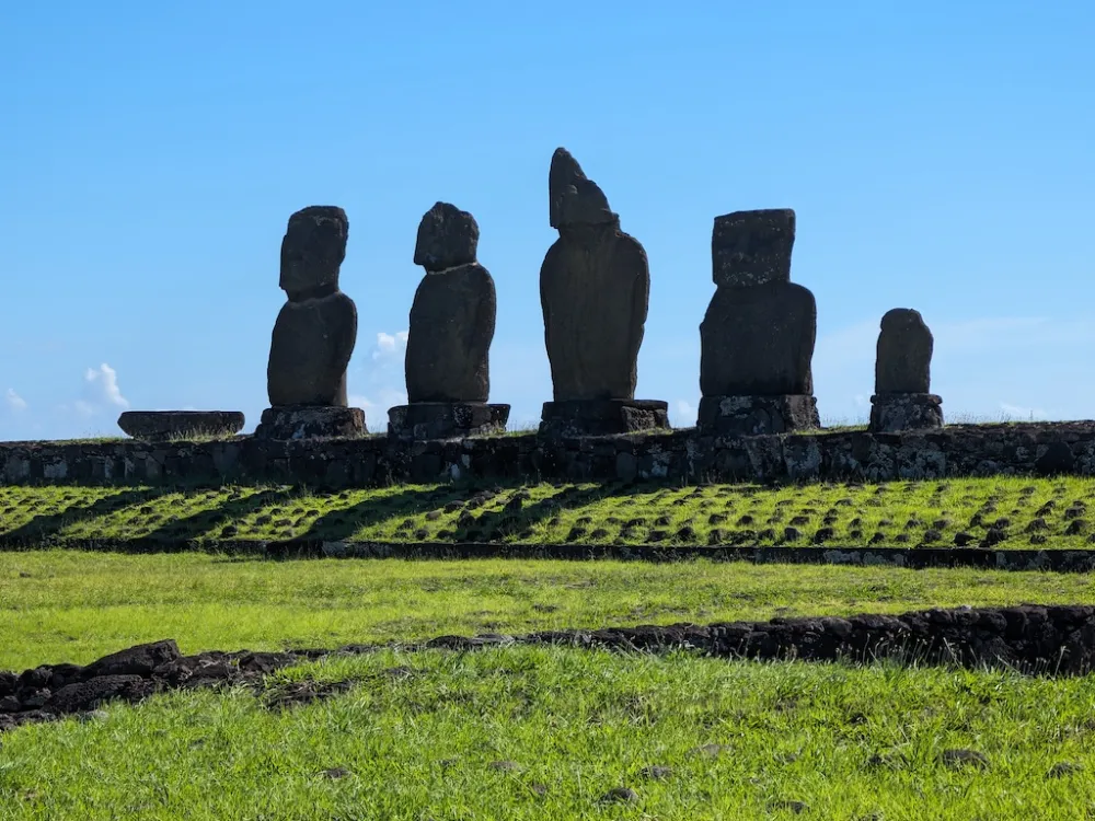 Five ancient moai stone statues standing on a raised stone platform on Rapa Nui, Chile, overlooking a grassy landscape beneath a clear blue sky.