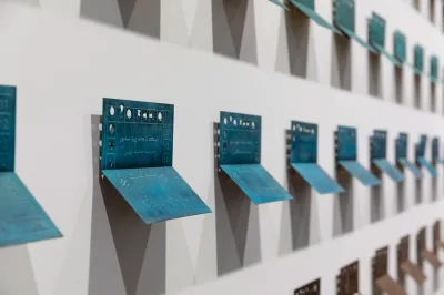 Installation view of bronze casts of bus tickets on a wall.