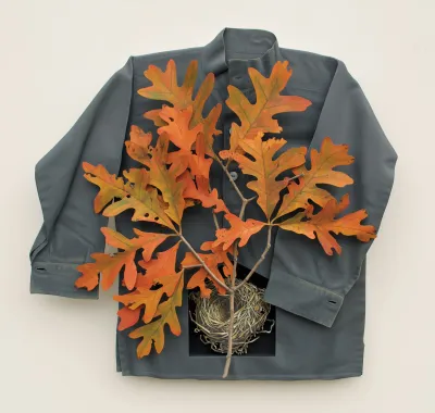 A sculptural painting featuring a gray shirt into which a nest is incised with orange leaves on top.
