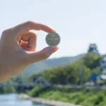 A photo shows a hand holding up a custom-made coin against a landscape background.