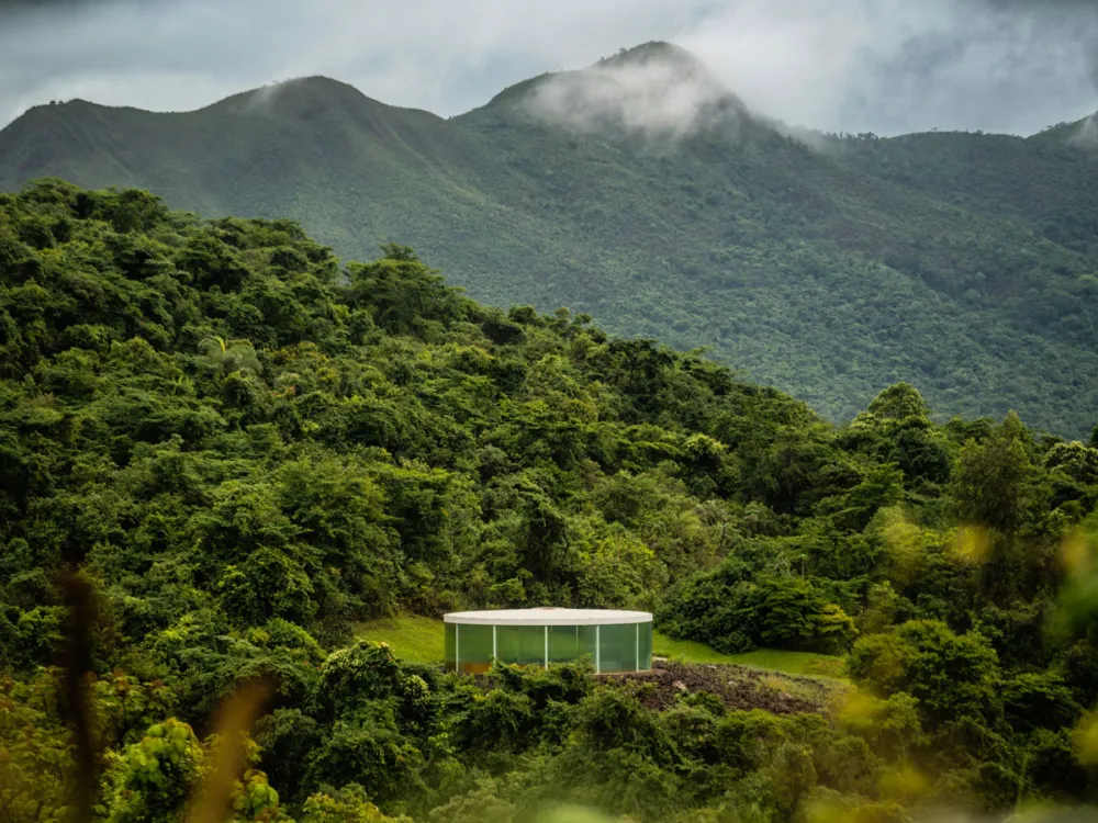 A lush Brazilian landscape with a small structure on a plateau in the center foreground.