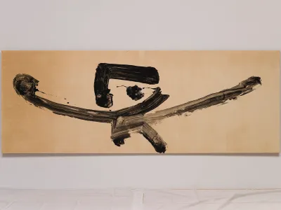 A painting of black ink, resembling calligraphy or Japanese characters, on a a cream-colored canvas.