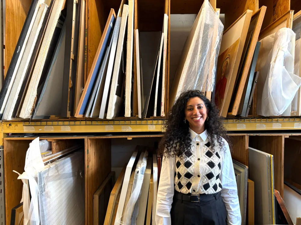 Portrait of Diya Vij in front of two shelves of frames.